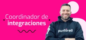 Un hombre sonríe con una sudadera negra con capucha que lleva la inscripción "puntored". A su lado se lee "Coordinador de integraciones" sobre un fondo rosa brillante.